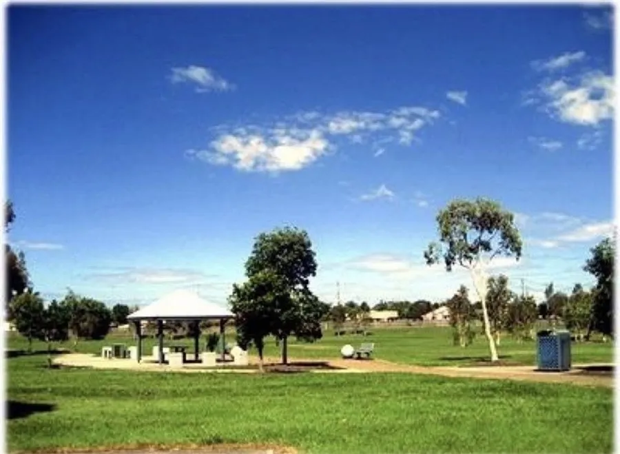 A park in Caboolture, Queensland, on a sunny day, with a small open pavilion, a eucalyptus tree and green grass under a blue sky.