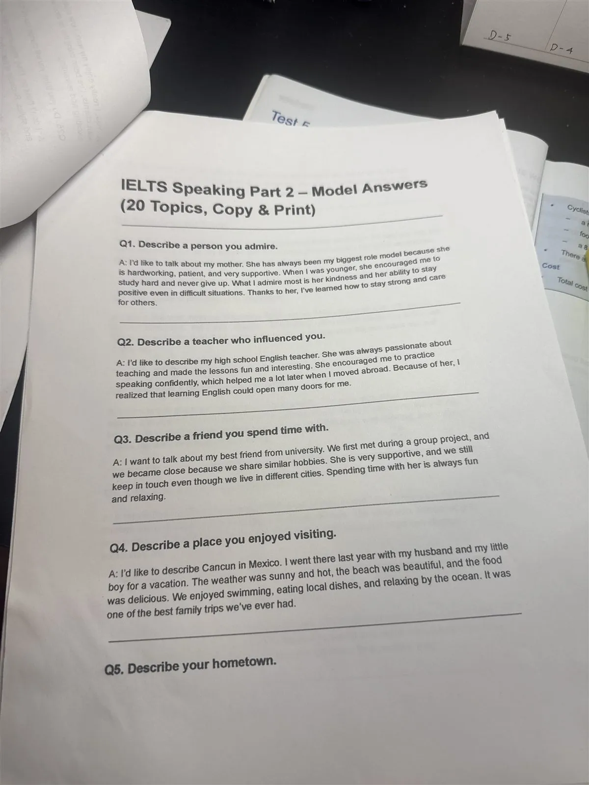 Printed IELTS speaking practice answers and practice books piled on a desk.